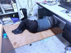 事務所の床で仮眠する平山